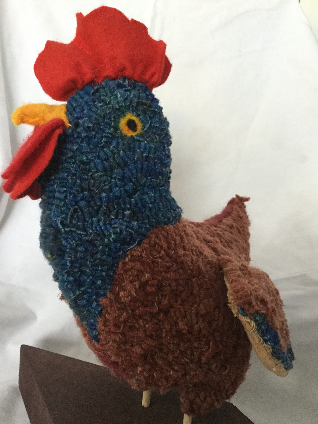 rug hooked hen sculpture with blue head and brown body. Sculpture is mounted on a wooden base